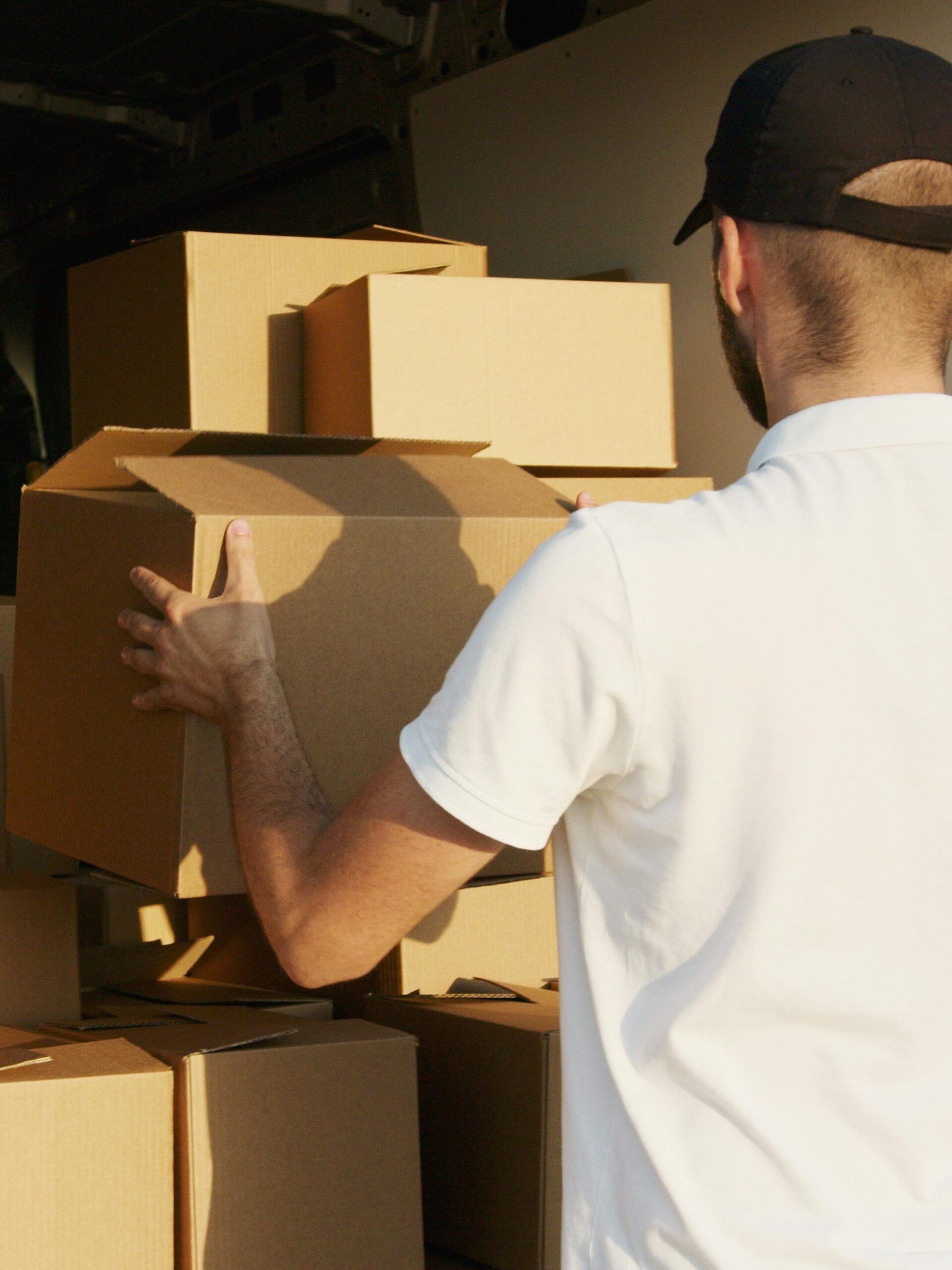 Home Courier arranging cardboard boxes in a delivery van during daytime.